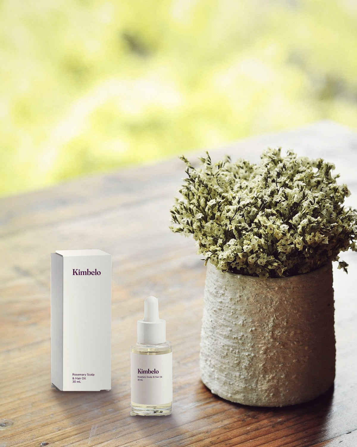 Kimbelo Rosemary Scalp & Hair Oil bottle and carton on a wooden table beside a potted plant